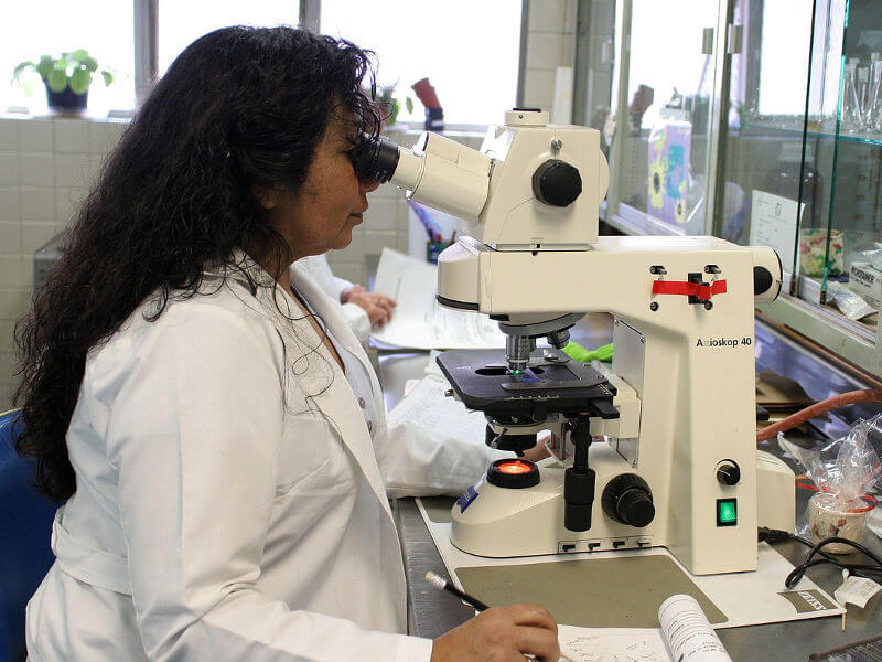 lady in white coat looking through a microscope