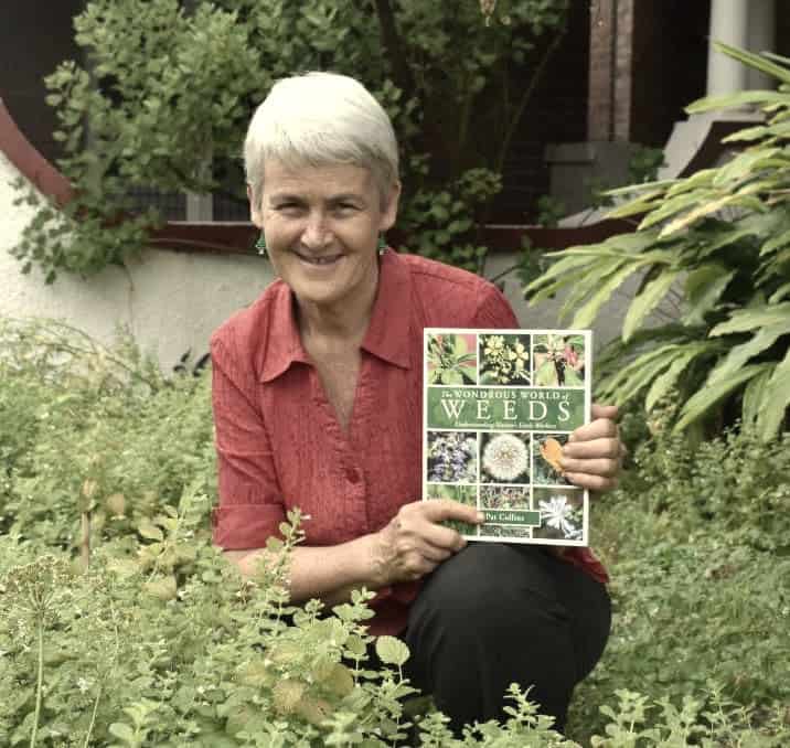 Pat in a garden holding her book on weeds