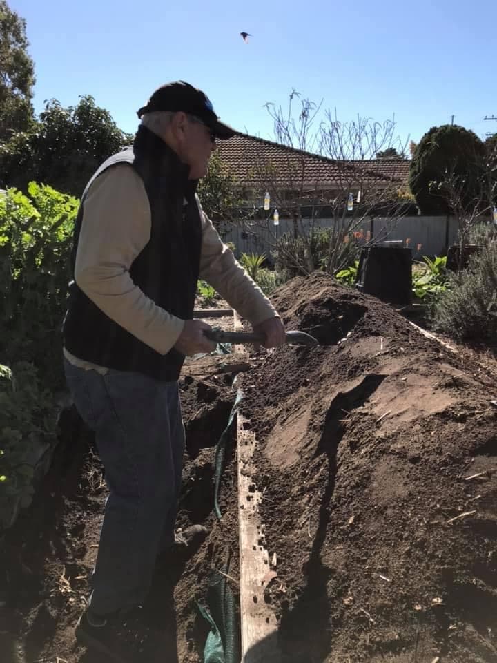 Man shovelling soil on a long hugelkultur mound